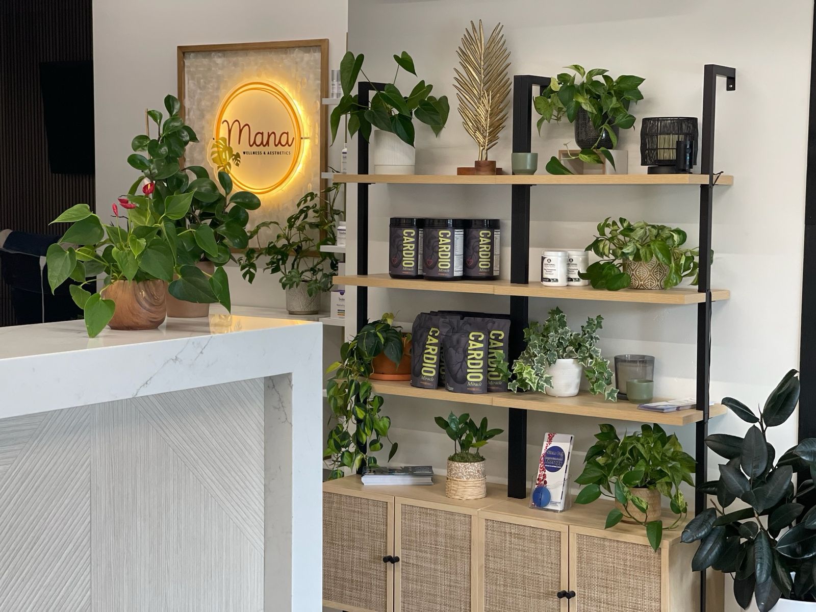 The bright Mana Wellness reception with plants and the glowing gold sign
